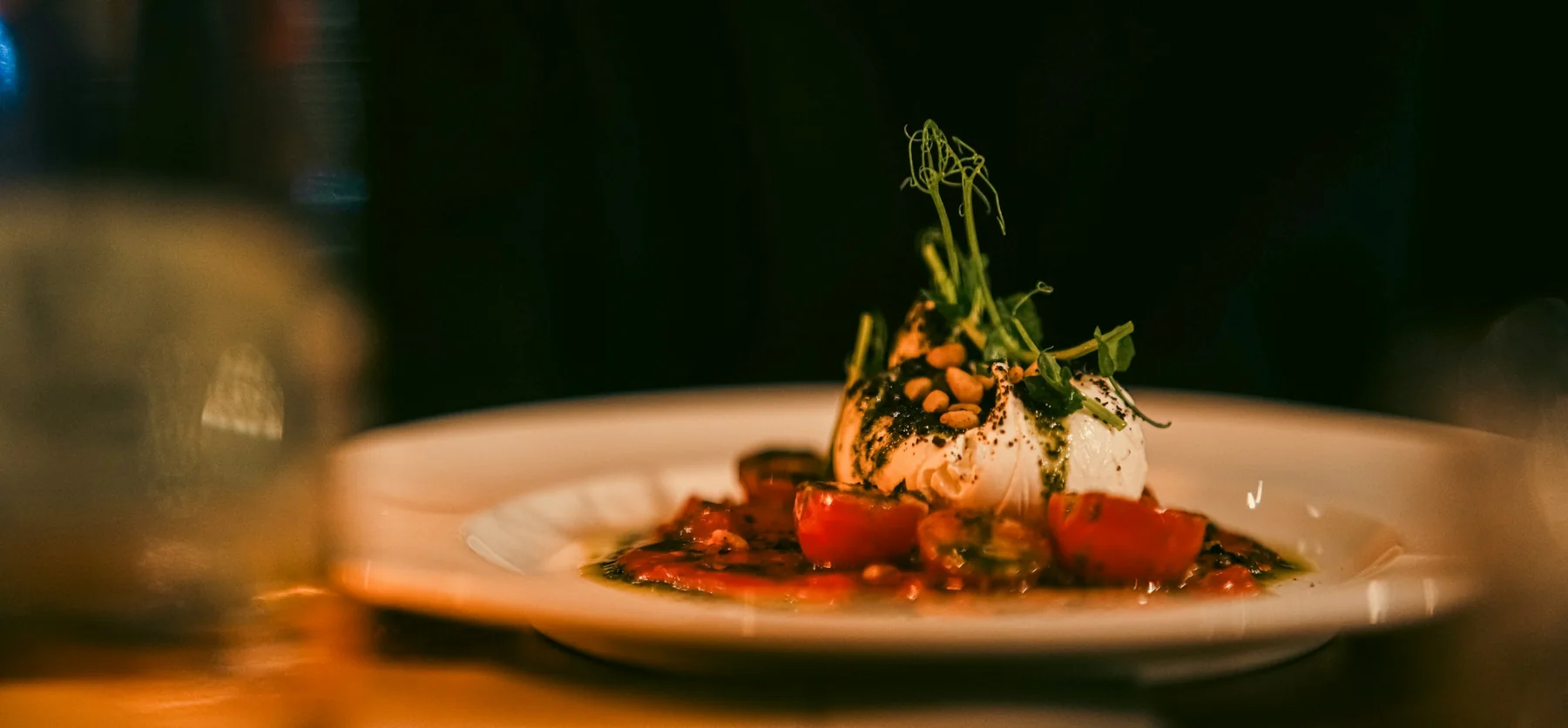Burrata, tomates et herbes fraîches dans une assiette, à la lumière chaude d’une salle à manger.